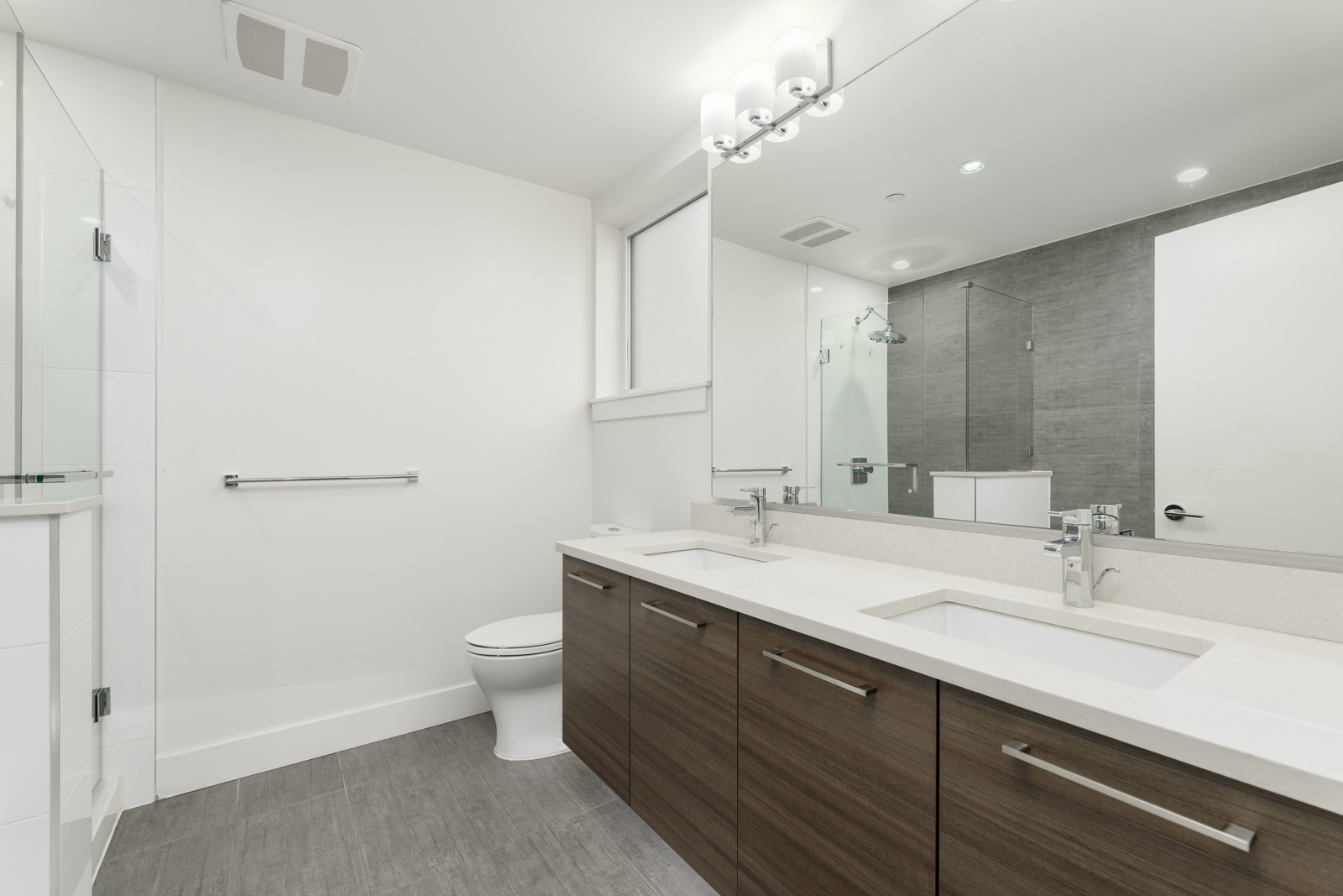 Modern bathroom with double sinks, large mirror, wooden cabinets, toilet, and a glass-enclosed shower.