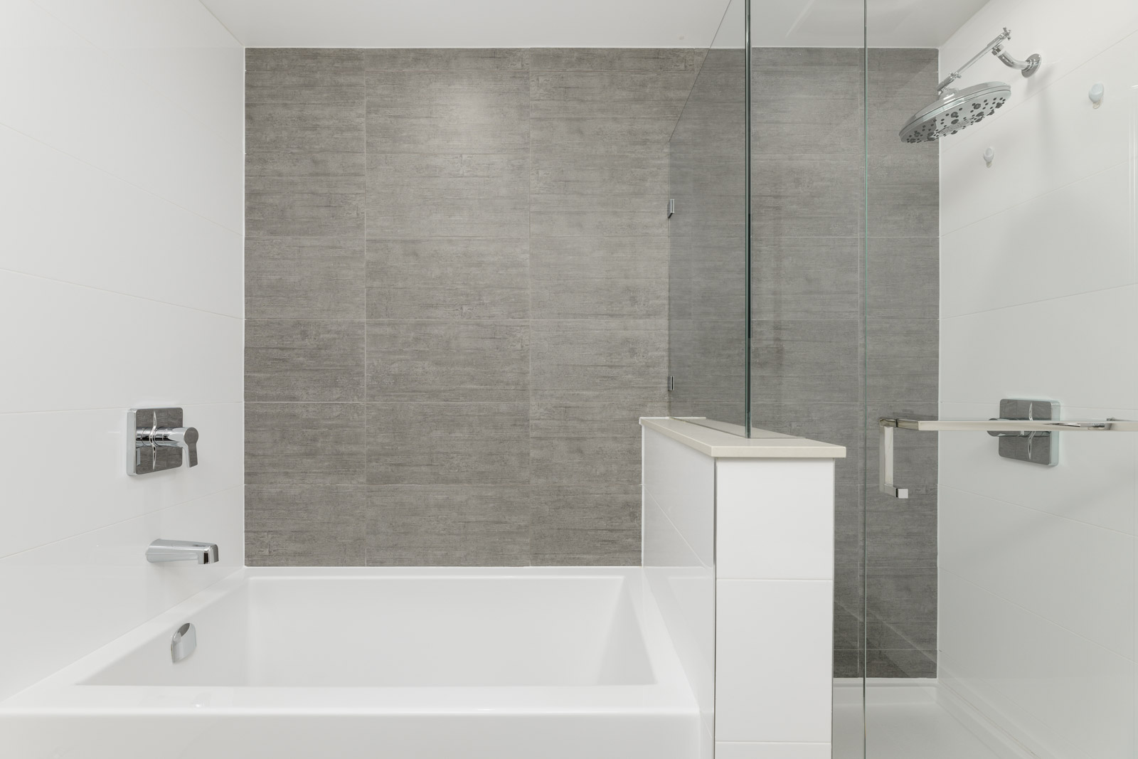 Minimalist bathroom with a white bathtub, glass shower enclosure, and gray tiled wall.