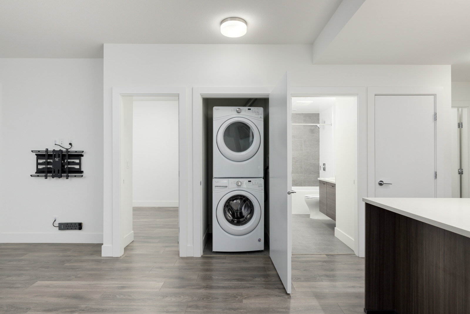 Interior of a modern room with a stackable washer and dryer in an open closet, flanked by doorways, and a mounted panel on the wall.