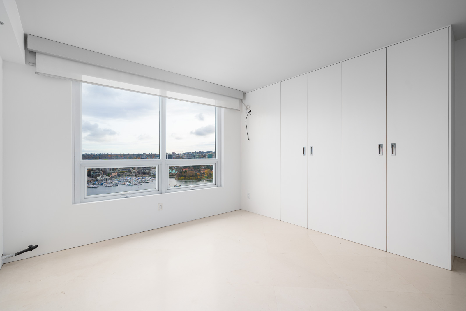 Empty room with a large window showing a scenic view, white walls, and built-in white cabinets.