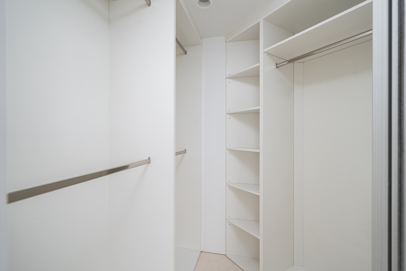 Empty white walk-in closet with hanging rods and shelves.