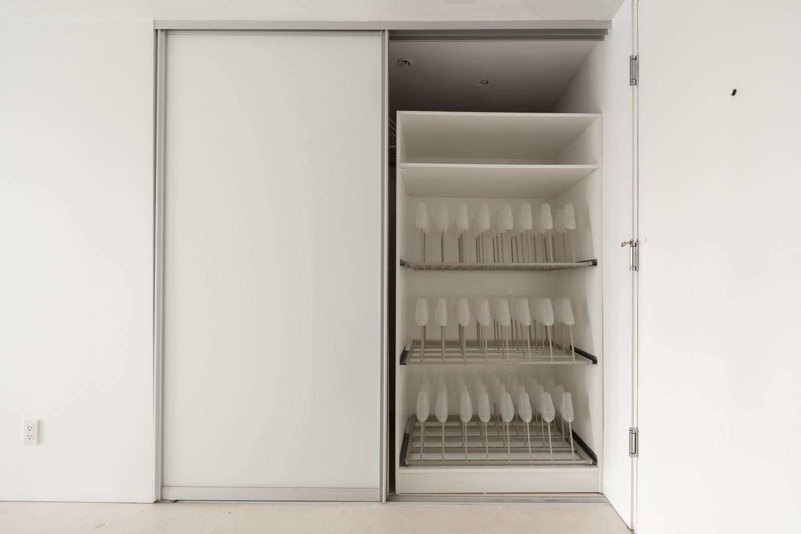 A closet with open sliding door reveals multiple rows of racks holding identical white chairs.