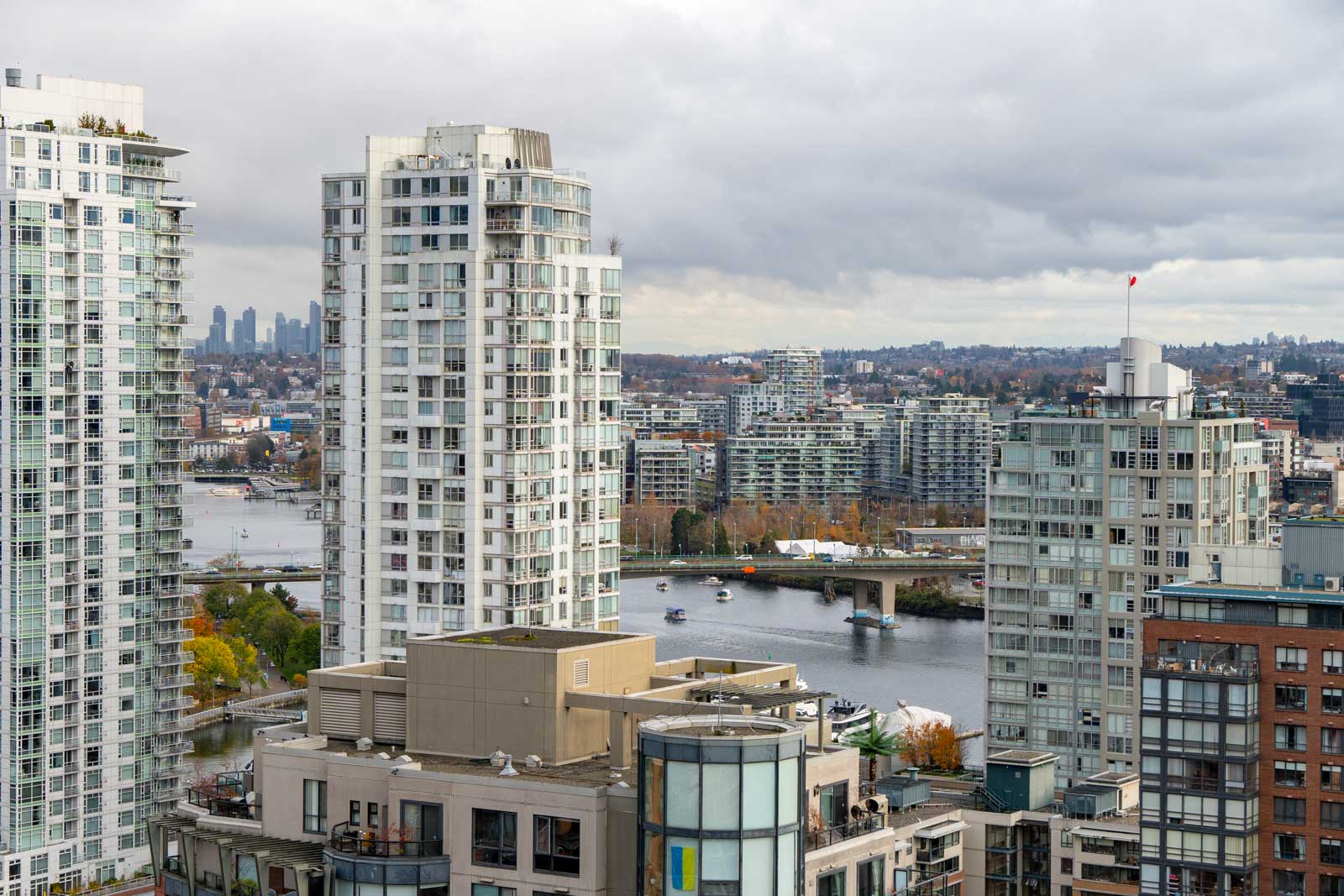 Cityscape view with tall residential buildings, a river with boats, and a distant skyline under a cloudy sky.
