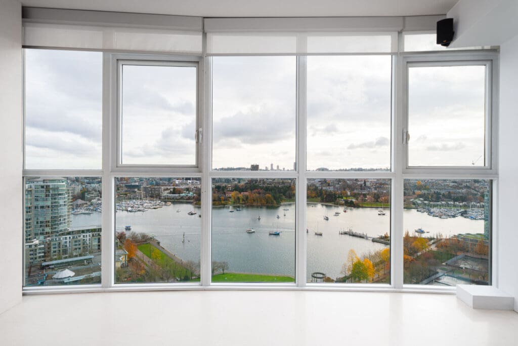 View from a large window overlooking a river, with boats and cityscape in the background under a cloudy sky.