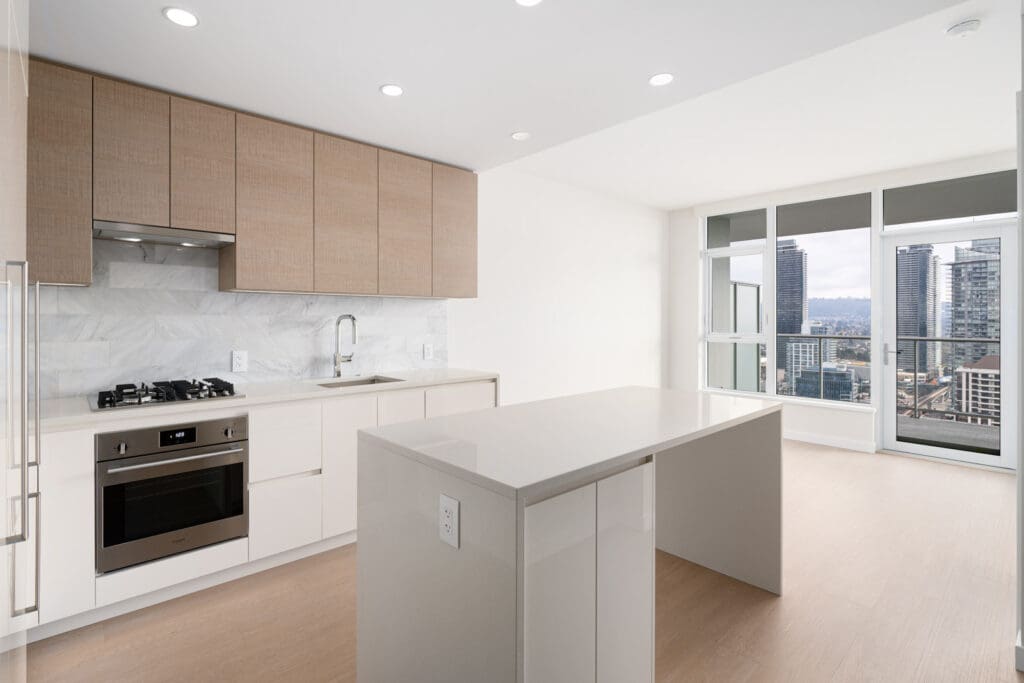 Modern kitchen with light wood cabinets, an island, and a built-in oven. Large windows offer a cityscape view.