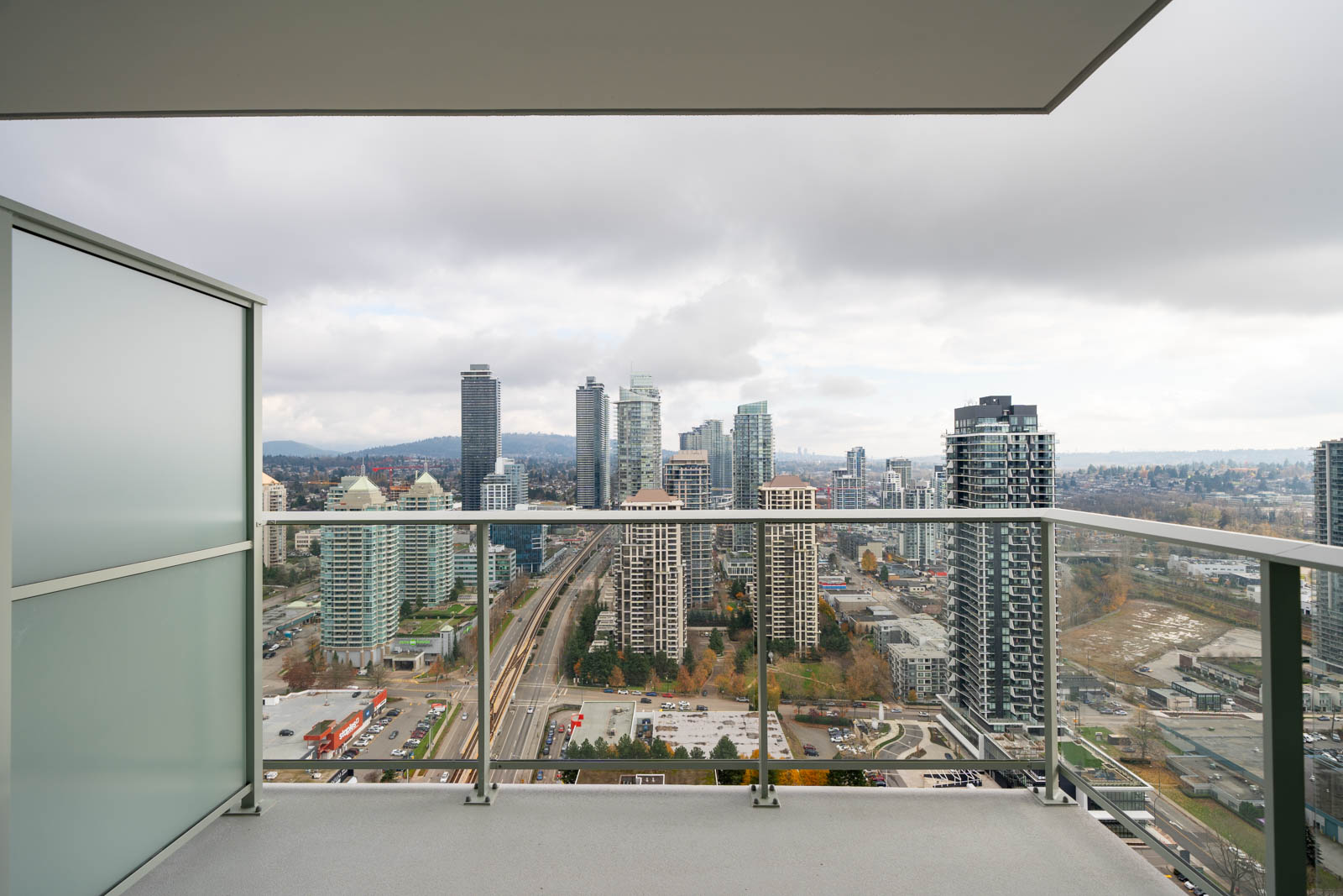 View from a balcony overlooking a cityscape with tall buildings, a railway, and cloudy sky.