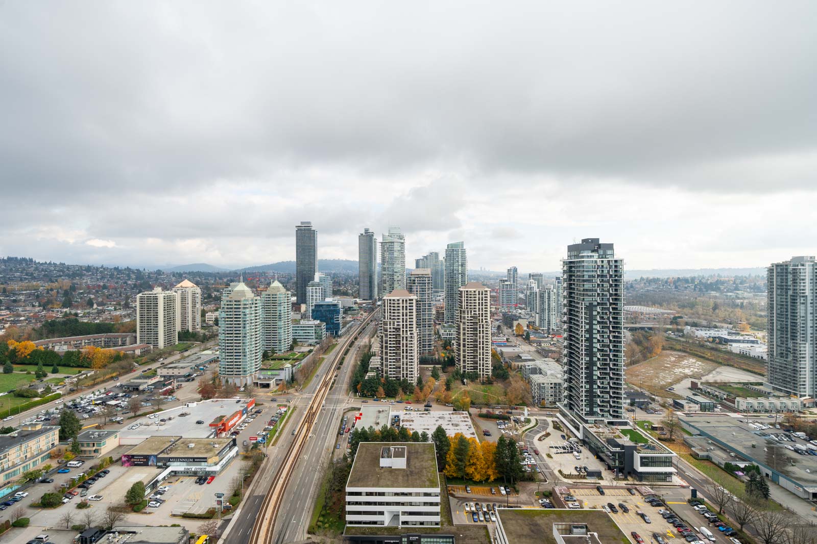 Aerial view of a cityscape with tall buildings, roads, and scattered trees under a cloudy sky.