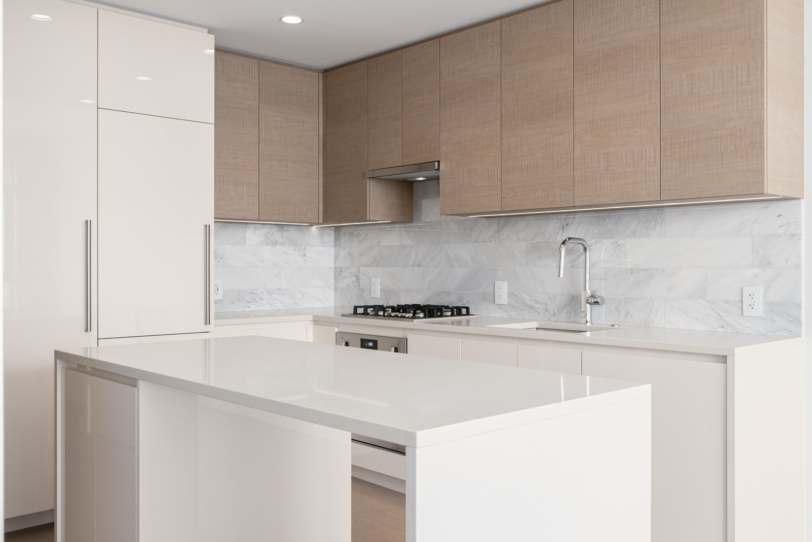 Modern kitchen with light wood cabinets, a marble backsplash, a gas stove, and a large white island countertop.