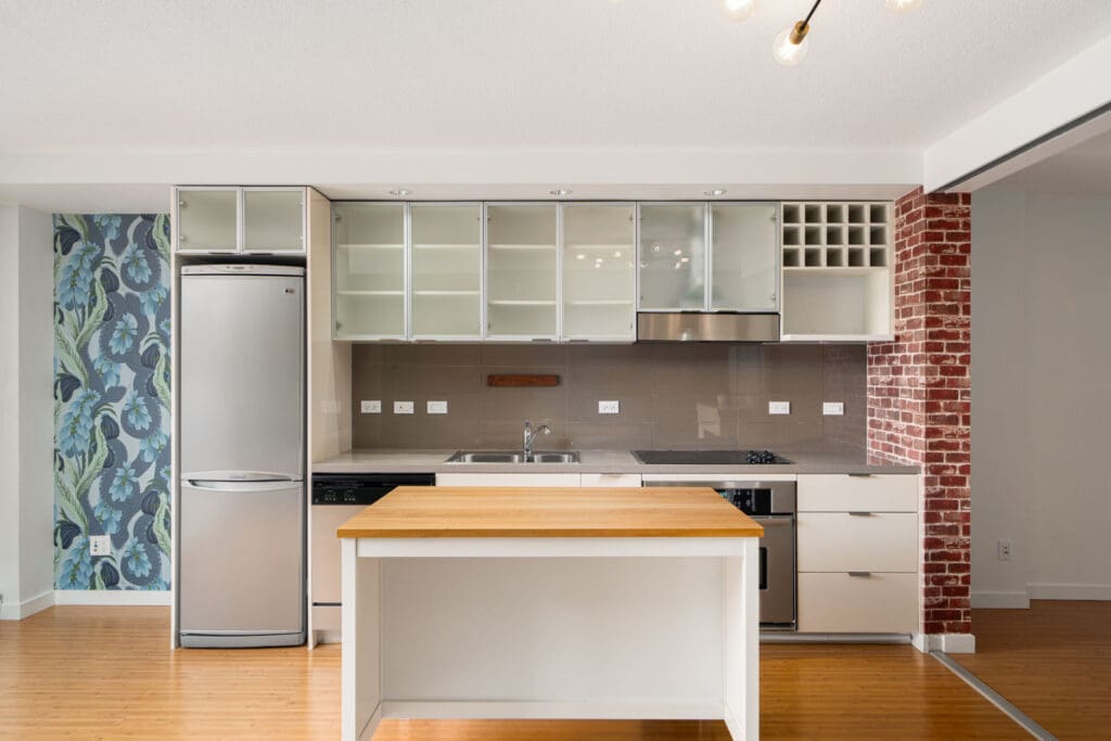 Modern kitchen with stainless steel appliances, a wooden island, glass cabinets, and a mix of floral and brick wallpaper accents.