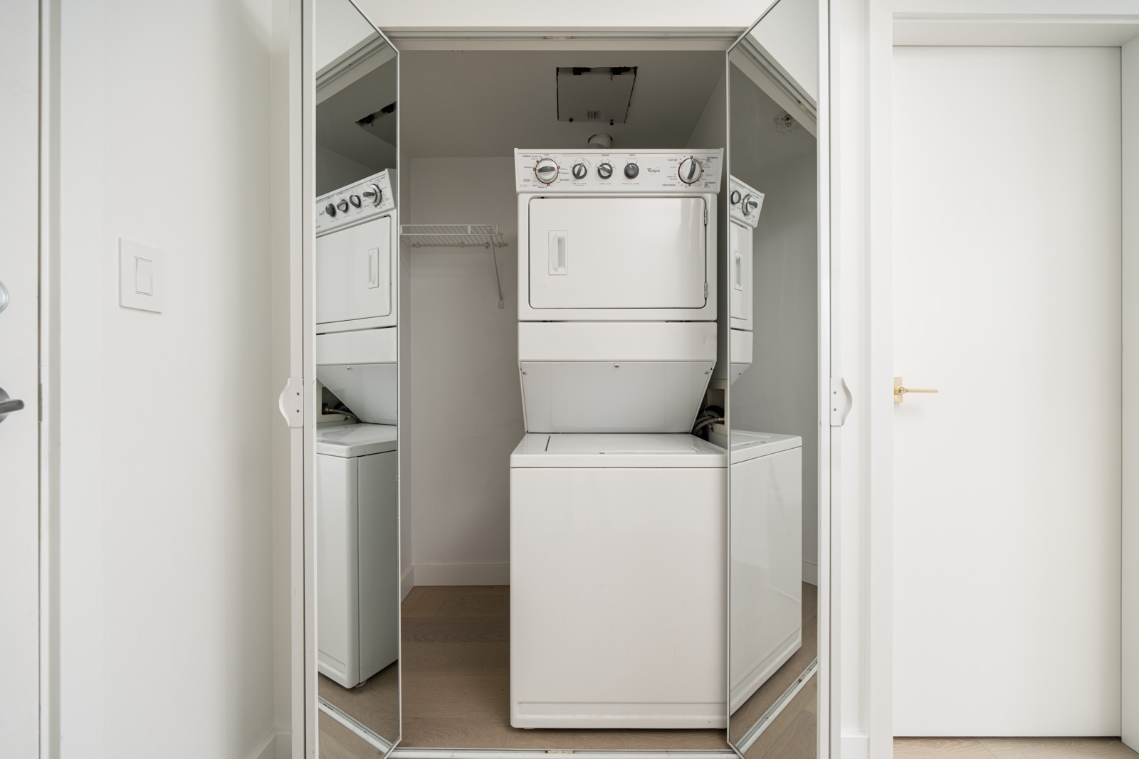 Stacked washer and dryer in a small, mirrored laundry room with a white wall and door.