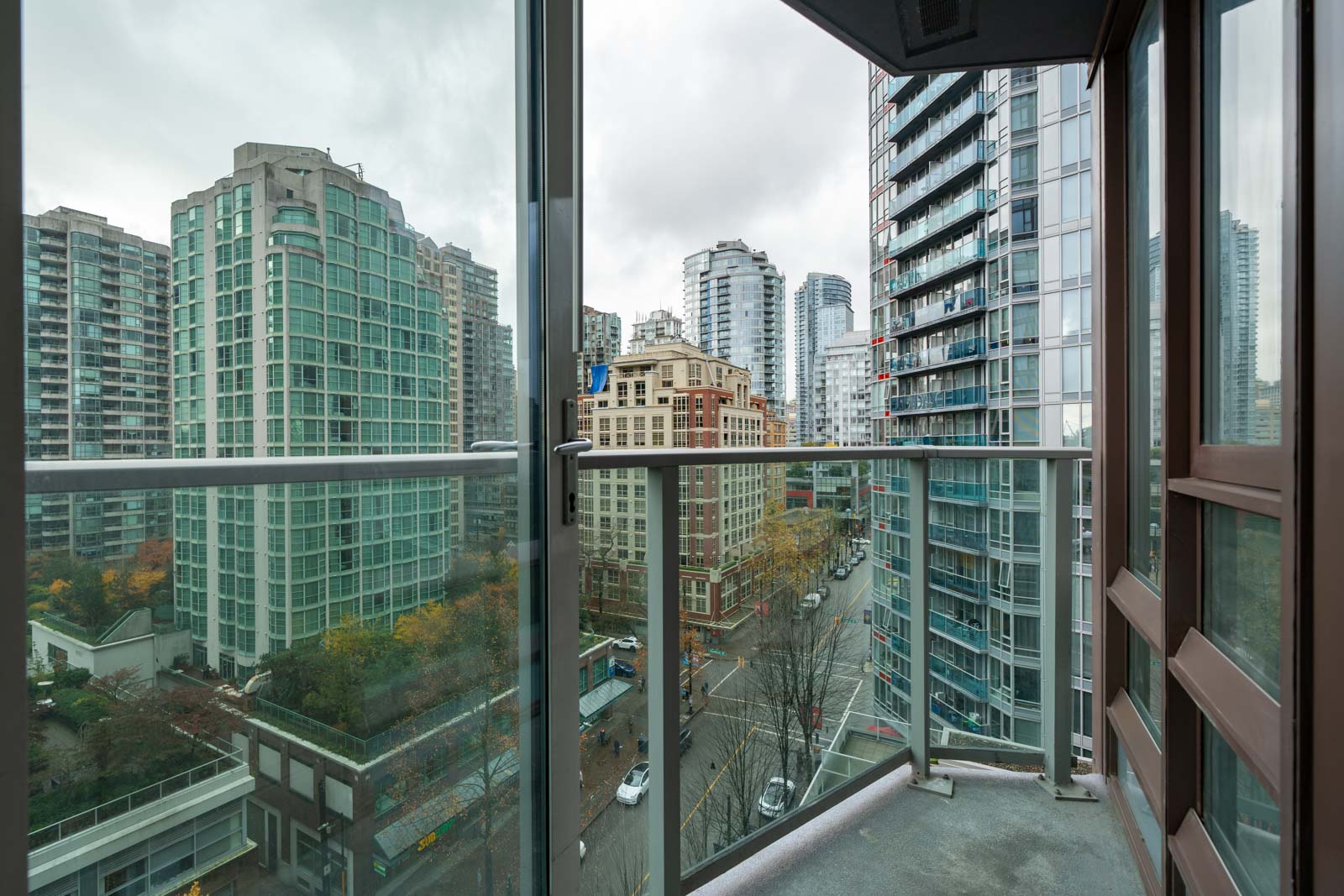 View from a balcony showing tall city buildings and a street below on an overcast day.