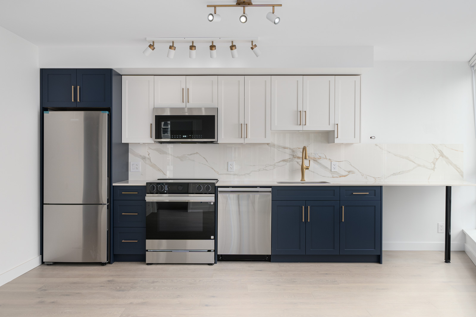 Modern kitchen with navy and white cabinets, stainless steel appliances, marble backsplash, and light wood flooring.