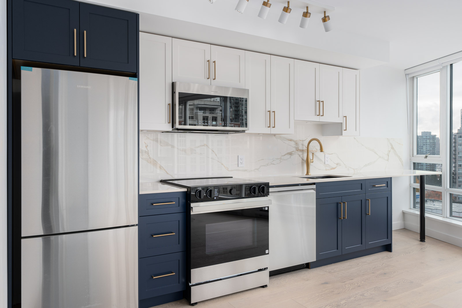 Modern kitchen with navy and white cabinets, stainless steel appliances, marble backsplash, and large windows overlooking a cityscape.
