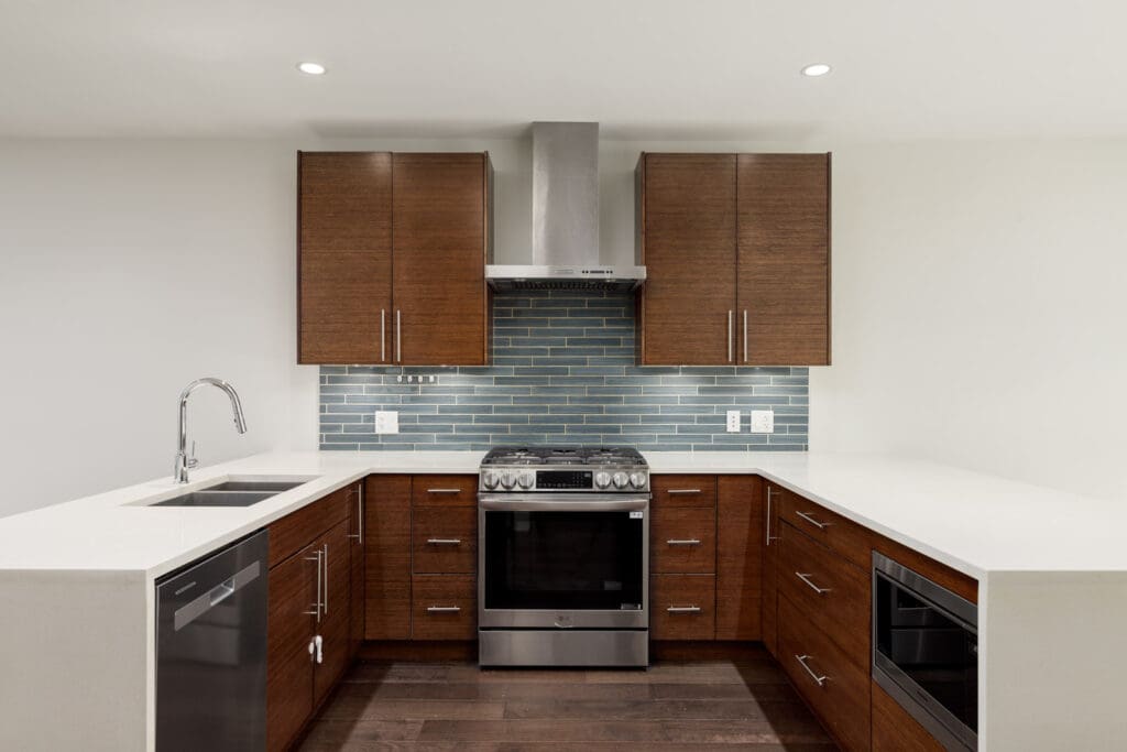 Modern kitchen with brown cabinets, stainless steel appliances, a tiled backsplash, and quartz countertops.