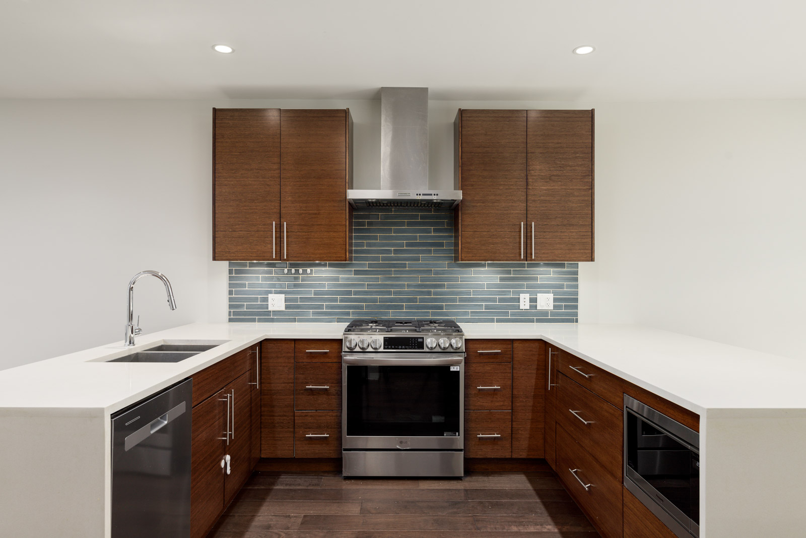 Modern kitchen with brown cabinets, stainless steel appliances, a tiled backsplash, and quartz countertops.