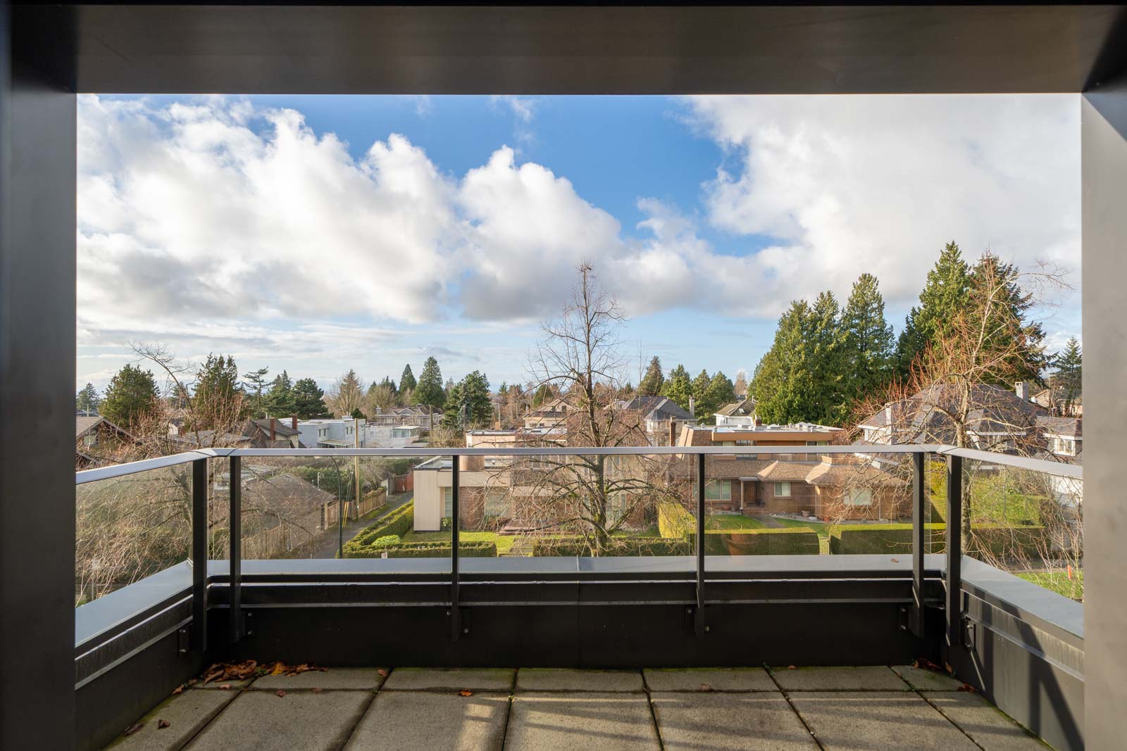 View from a balcony overlooking suburban houses, trees, and a partly cloudy sky.