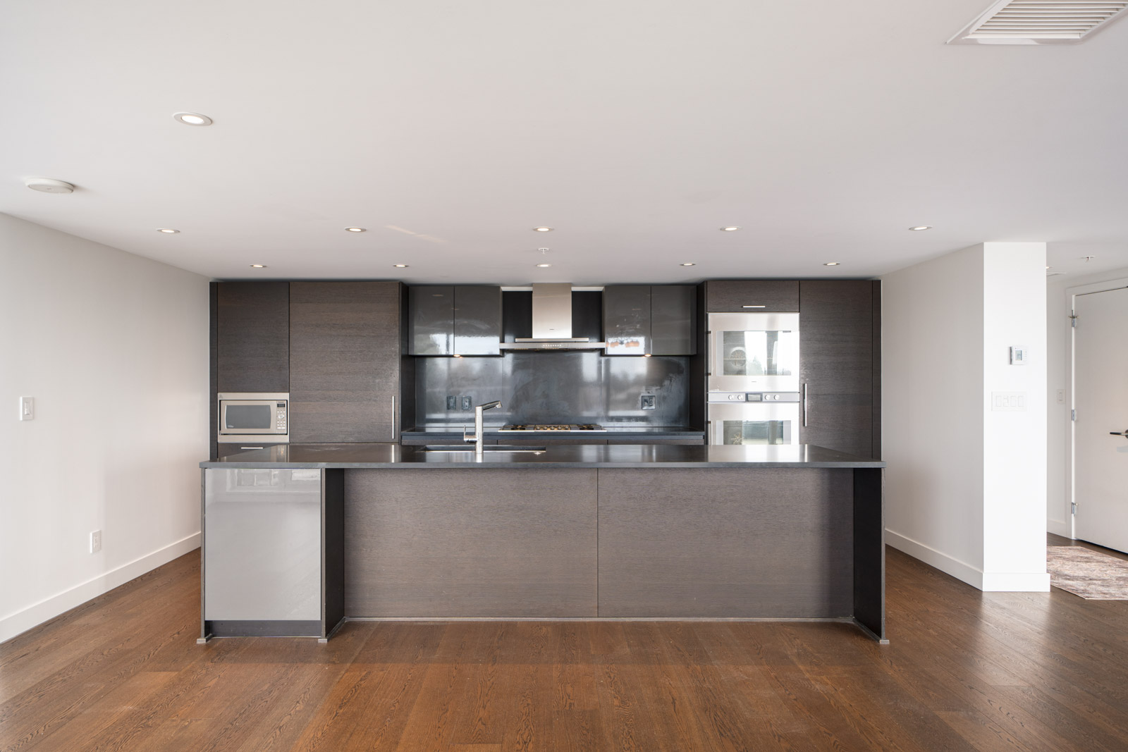 Modern kitchen with dark wood cabinets, an island counter, stainless steel appliances, and hardwood flooring.