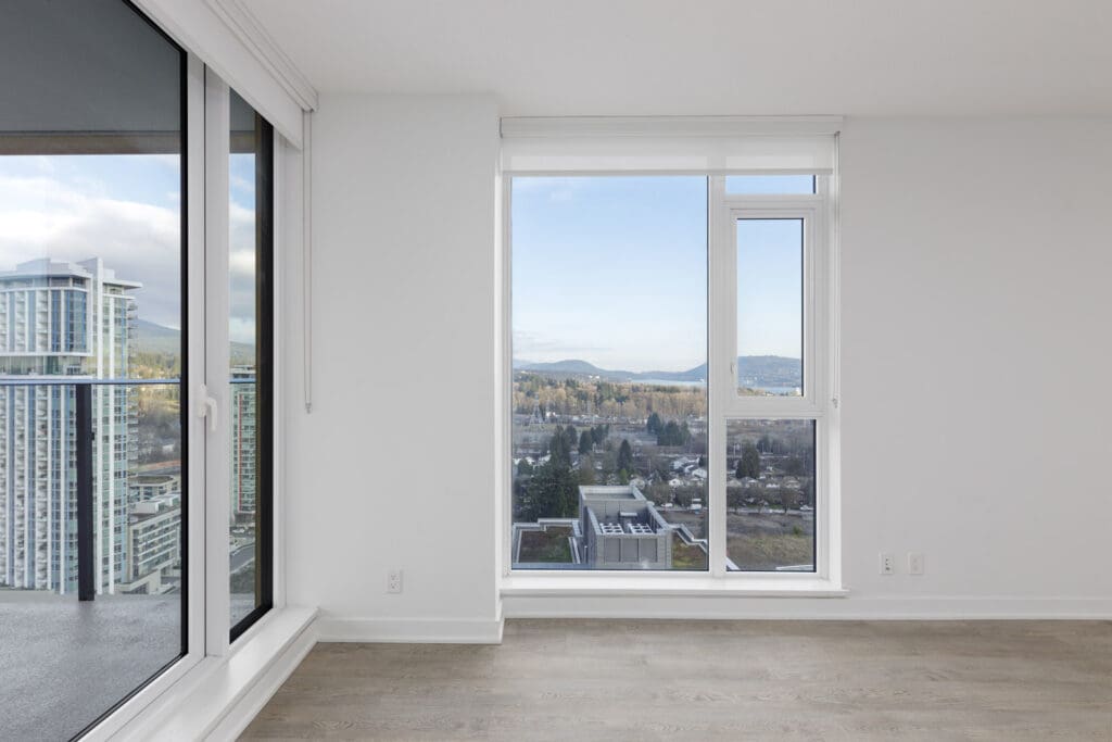 Empty room with large windows, grey flooring, offering a view of buildings and distant mountains.