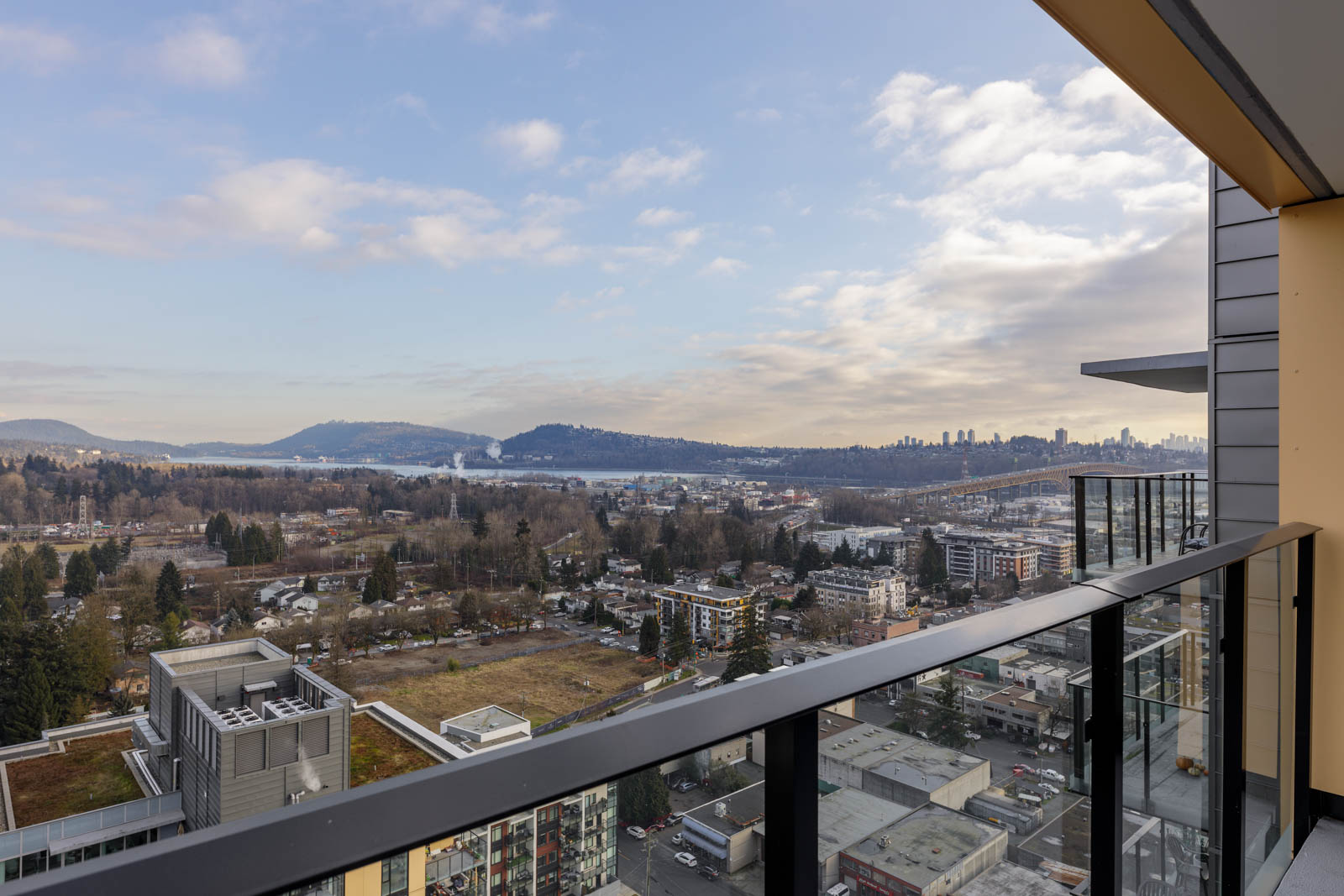 View from a balcony showing a cityscape with scattered buildings, hills in the distance, and a cloudy sky.