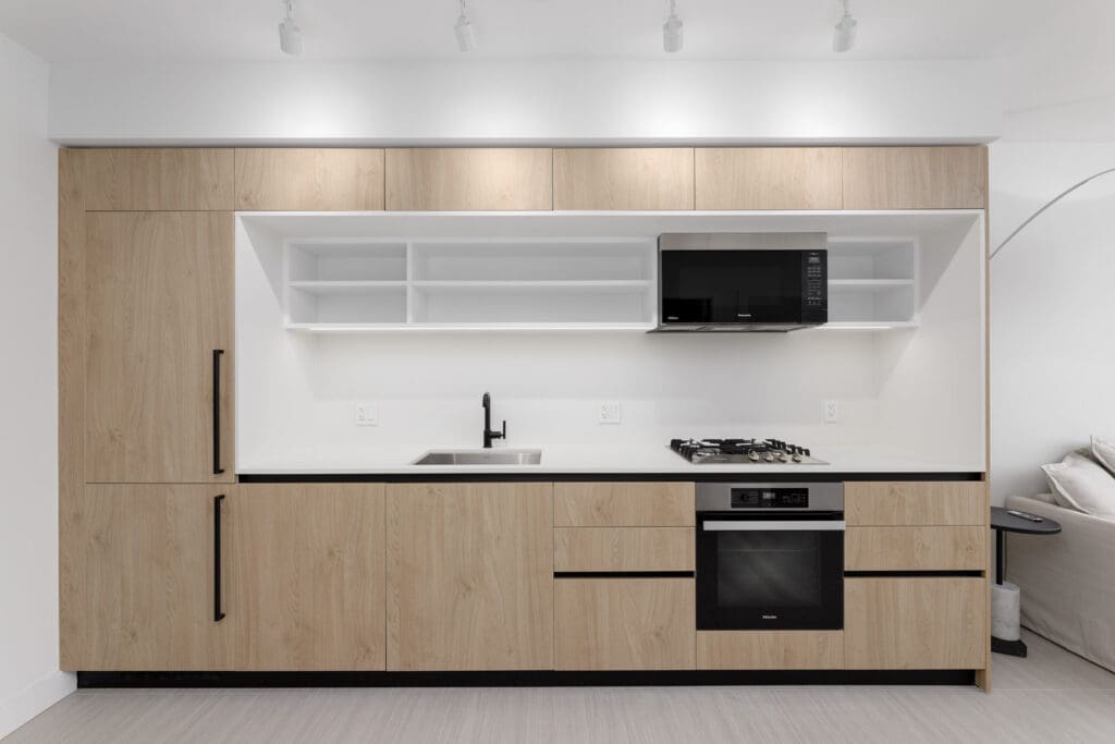 Modern kitchen with wooden cabinets, a built-in oven, microwave, and stovetop. There is a sink with a faucet and open shelving above the counter.