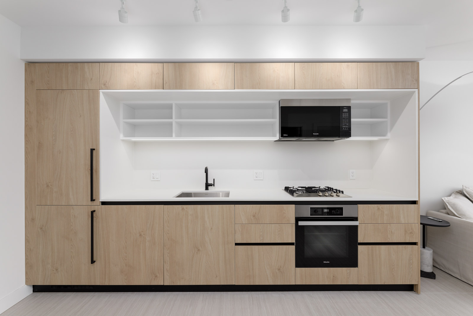 Modern kitchen with wooden cabinets, a built-in oven, microwave, and stovetop. There is a sink with a faucet and open shelving above the counter.