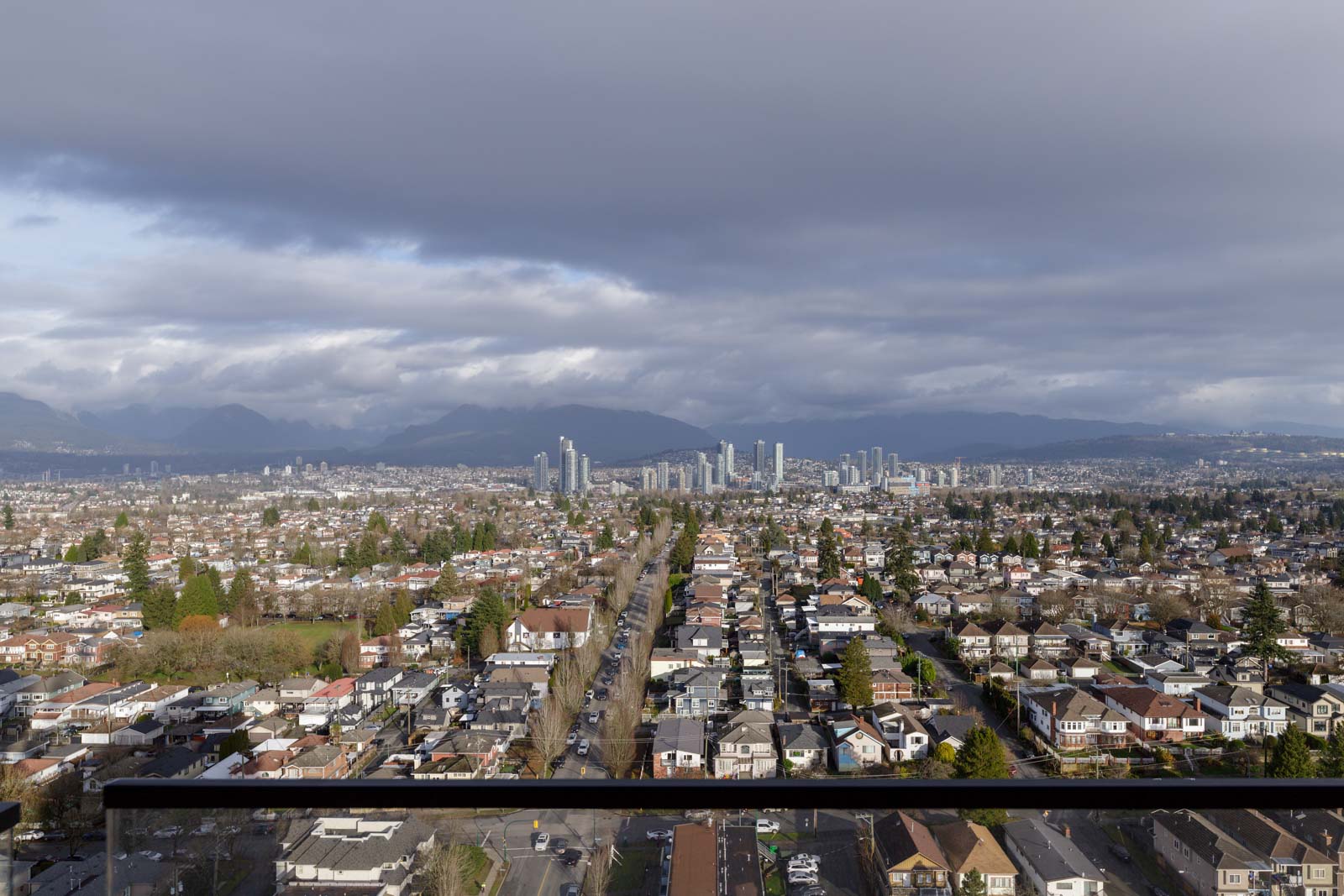 Aerial view of a cityscape with a cloudy sky, featuring rows of residential houses in the foreground and tall buildings in the background.