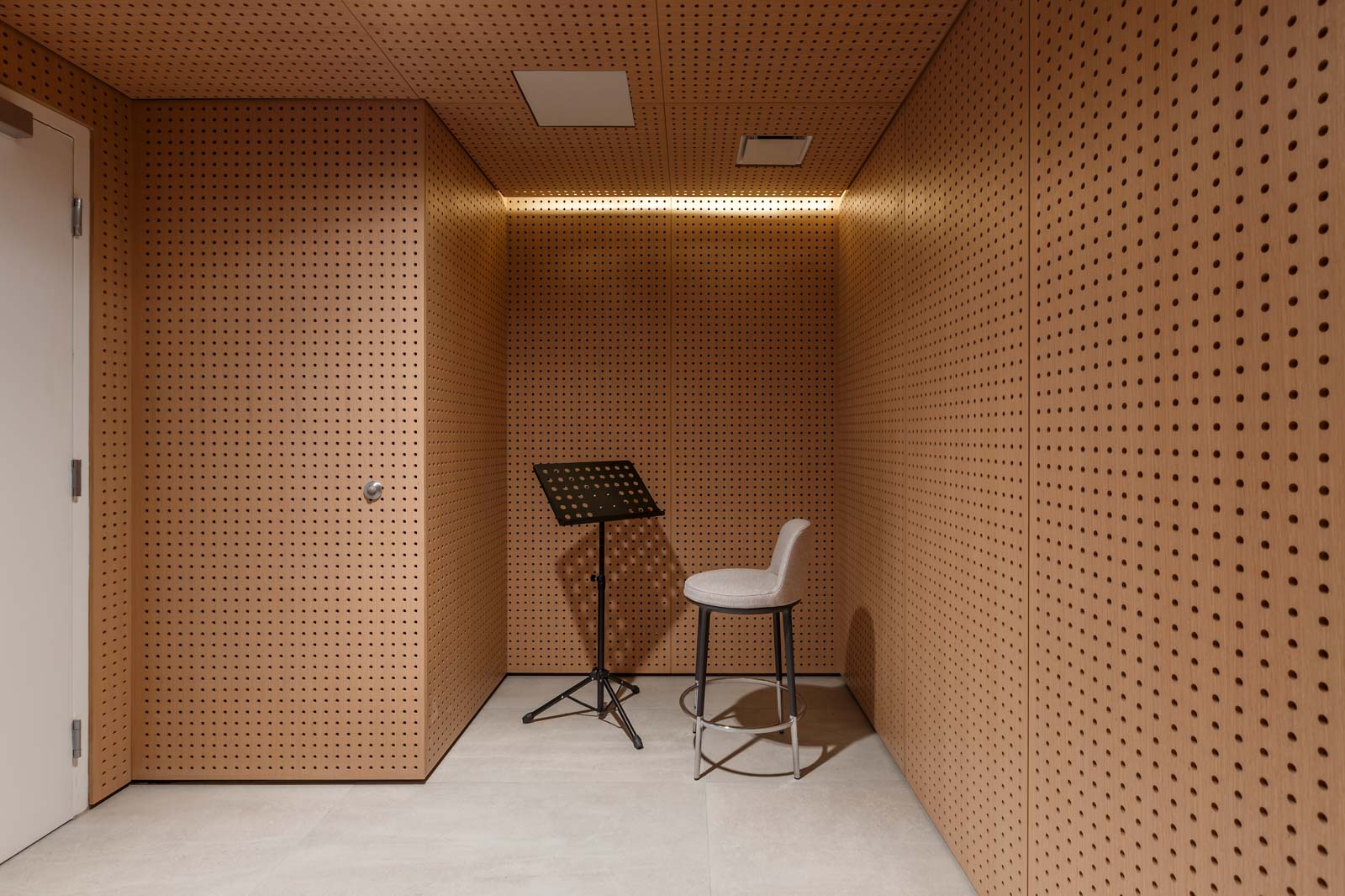 A small, soundproof room with wooden perforated walls features a music stand and a stool.