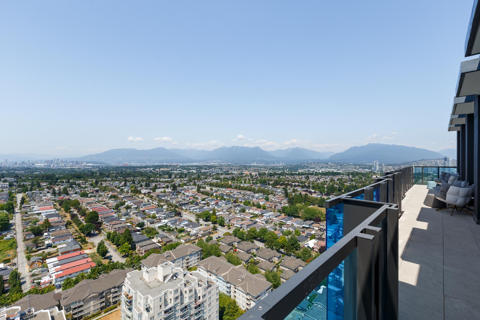 Aerial view from a high-rise balcony overlooking a cityscape with residential areas, distant mountains, and a clear sky.