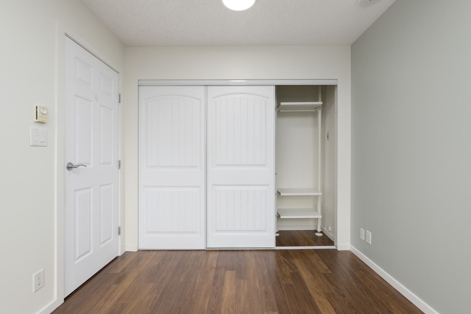 Empty room with a closet featuring sliding doors, hardwood floor, and white walls.