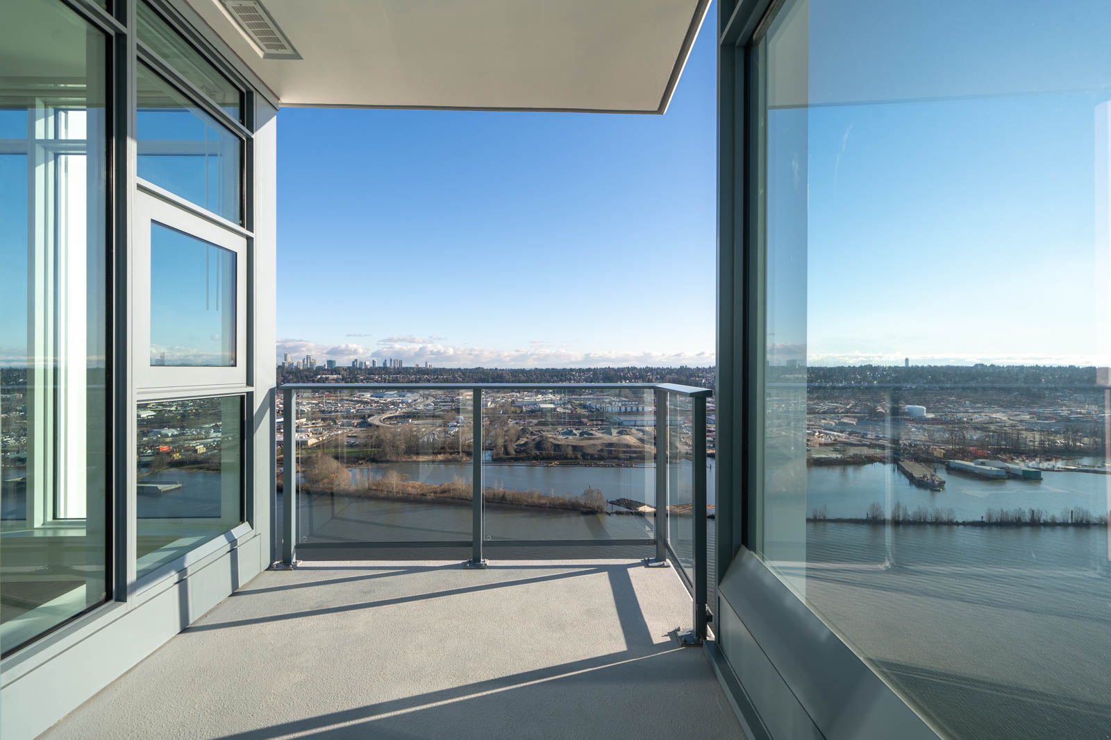 Glass balcony overlooking a cityscape with a river and distant skyline under a clear blue sky.