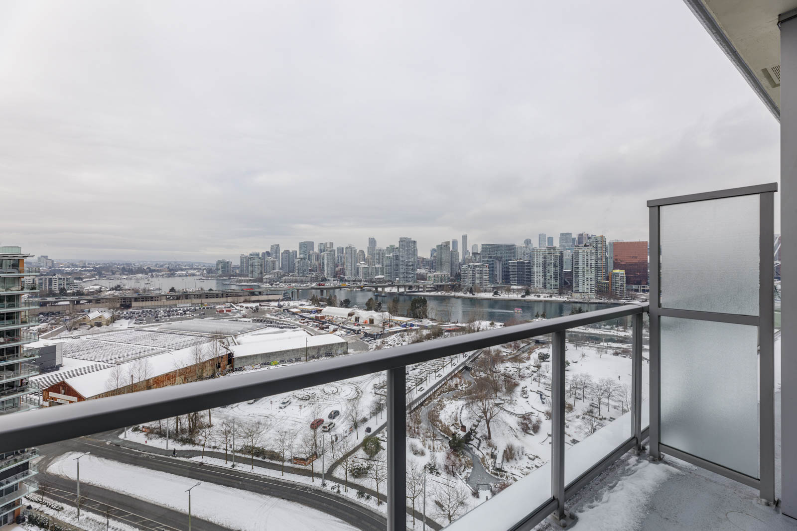 View from a balcony showing a snowy cityscape with high-rise buildings and a river on a cloudy day.