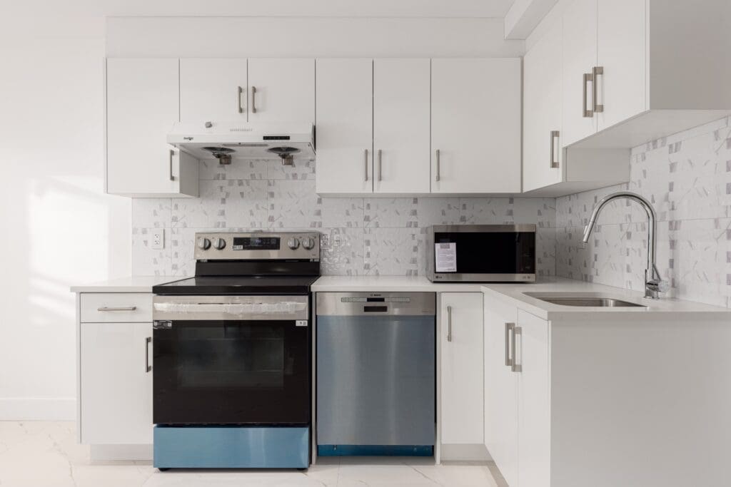 Modern kitchen with white cabinets and tiled backsplash. Features a stainless steel stove, dishwasher, and microwave.