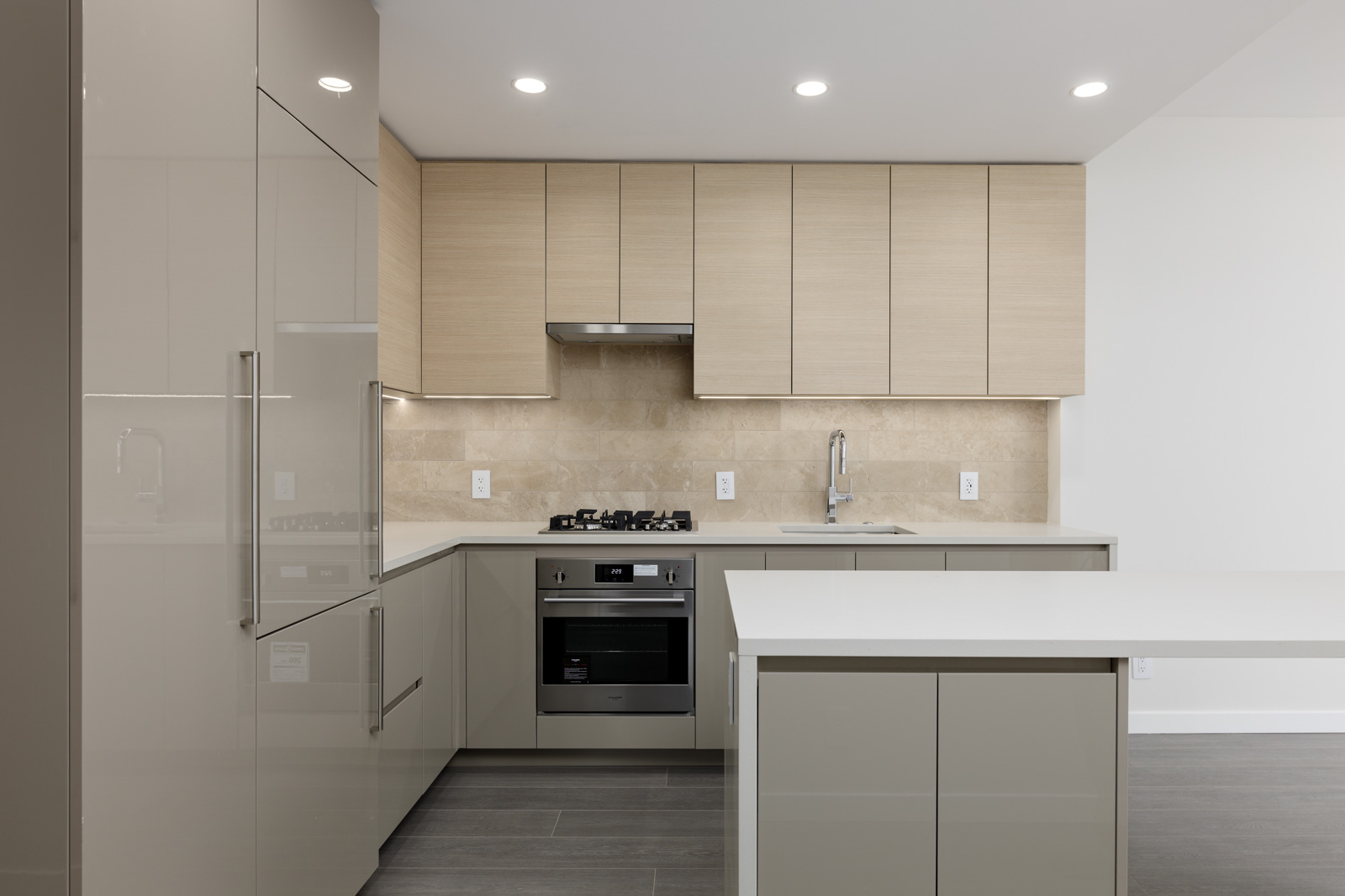 Modern kitchen with beige cabinets, stainless steel appliances, and a tiled backsplash. Features a built-in oven, gas stove, and an island counter with an overhead light.