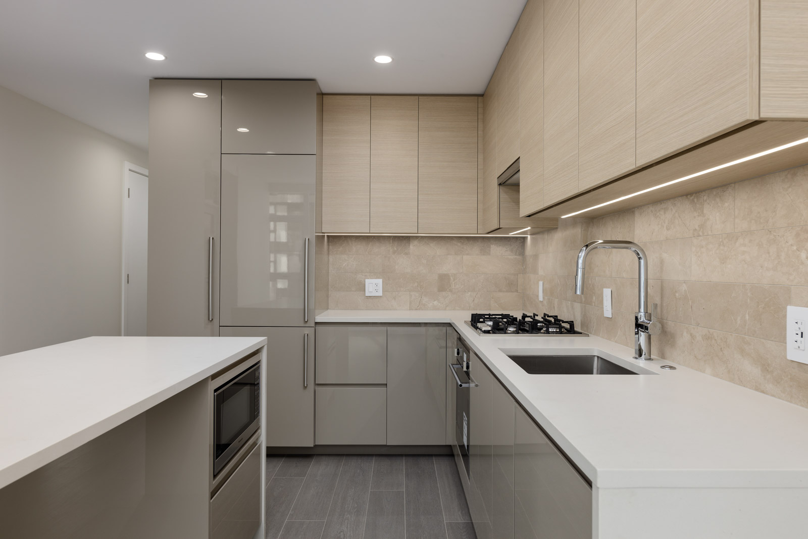 Modern kitchen with beige cabinets, white countertops, gas stove, and built-in appliances. Neutral tile backsplash and recessed lighting enhance the space.