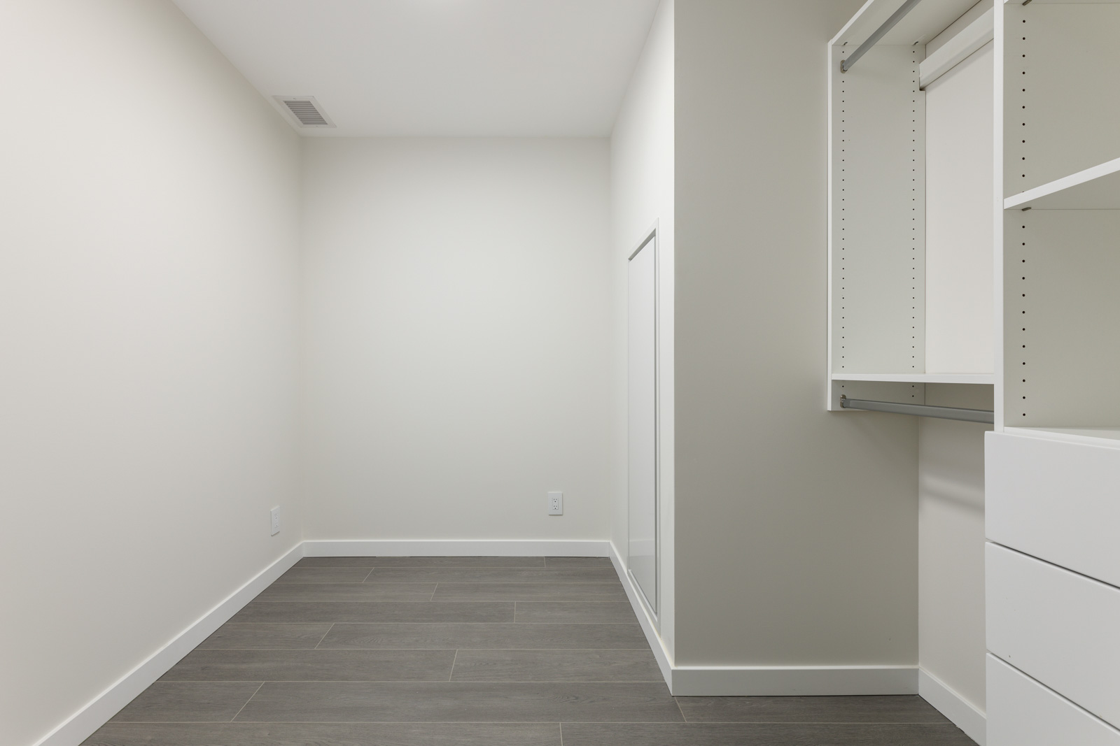 Empty walk-in closet with white walls, gray tiled floor, and built-in shelving on the right.