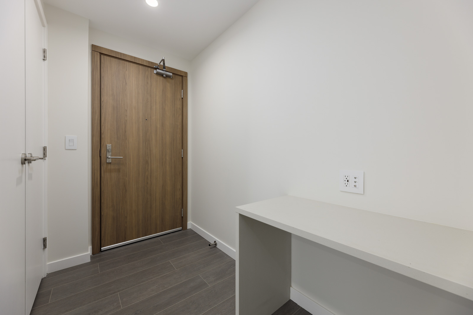 Minimalist hallway with light walls, a wooden door, gray tile floor, and a built-in white shelf.