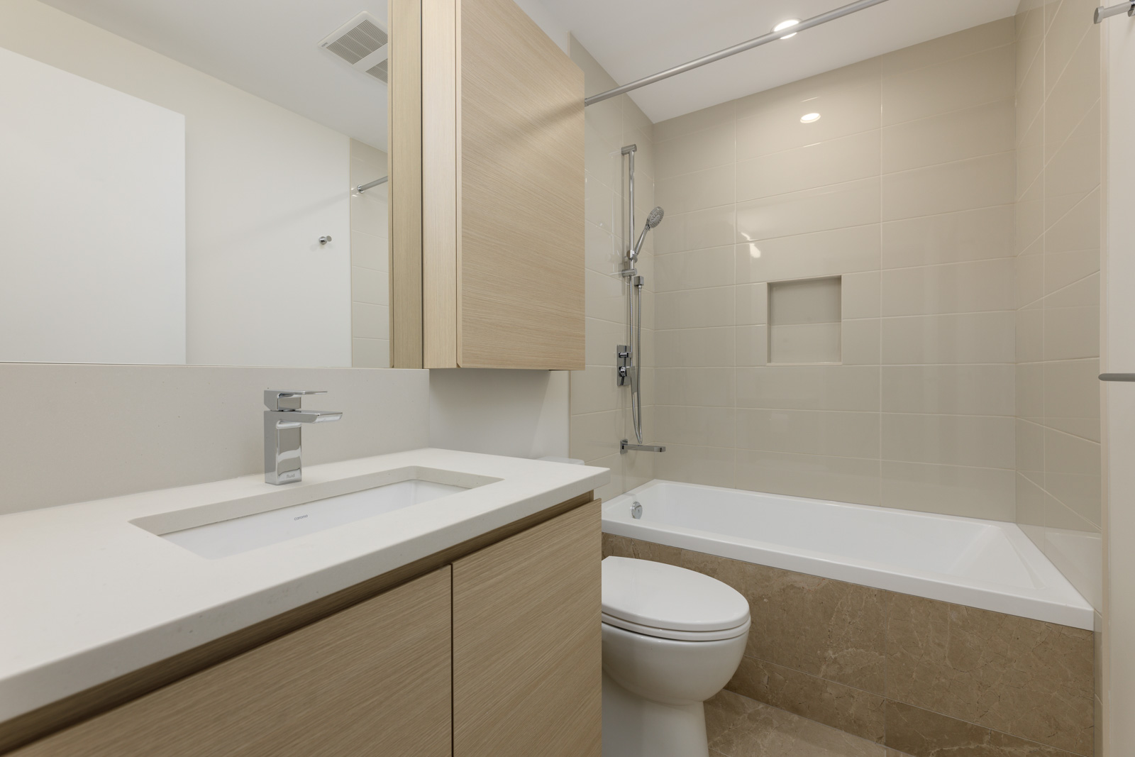 Modern bathroom with beige tiles, a bathtub with a showerhead, a vanity with a rectangular sink, and a wall-mounted mirror cabinet.