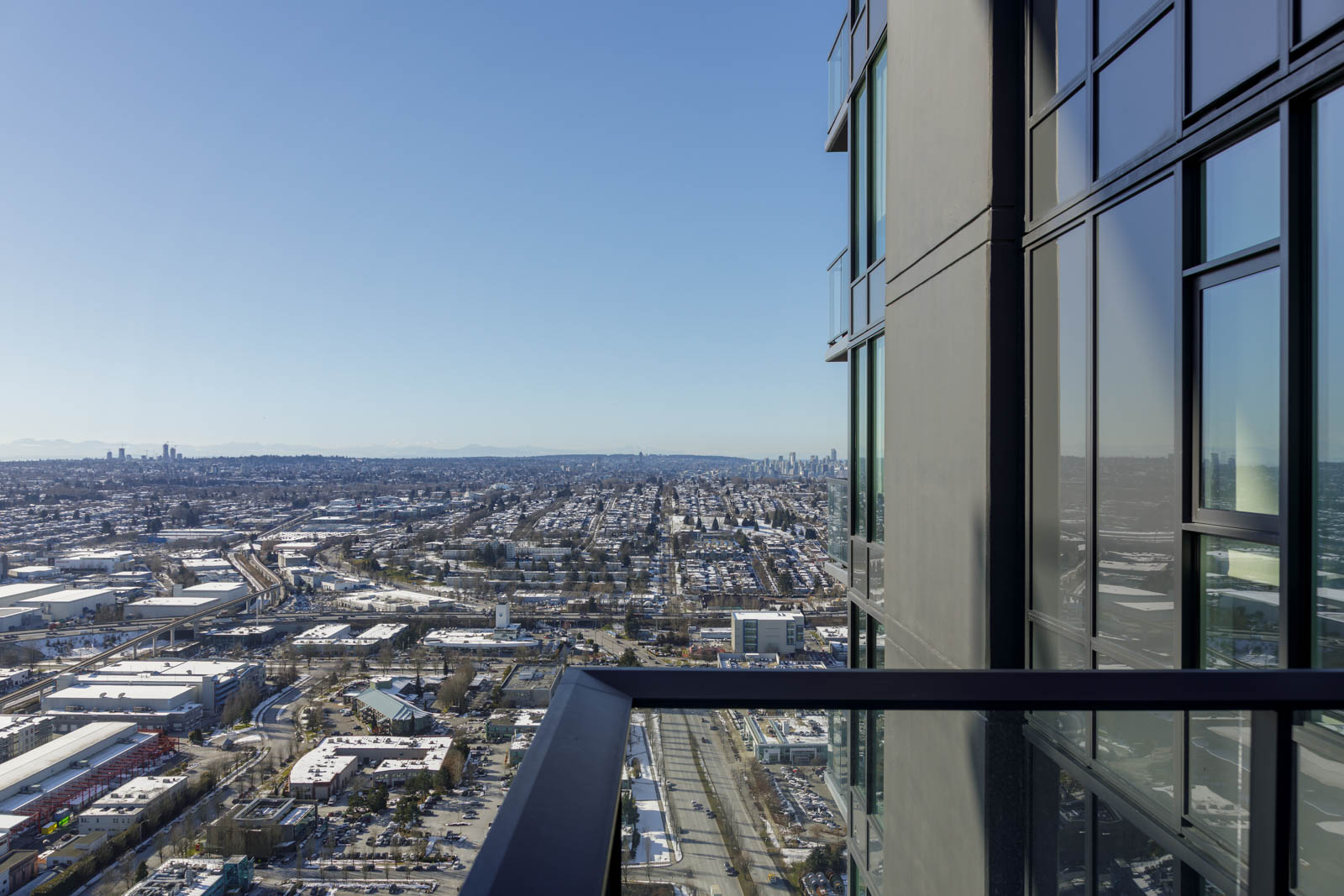 View from a high-rise balcony overlooking a sprawling urban landscape with buildings under a clear blue sky.