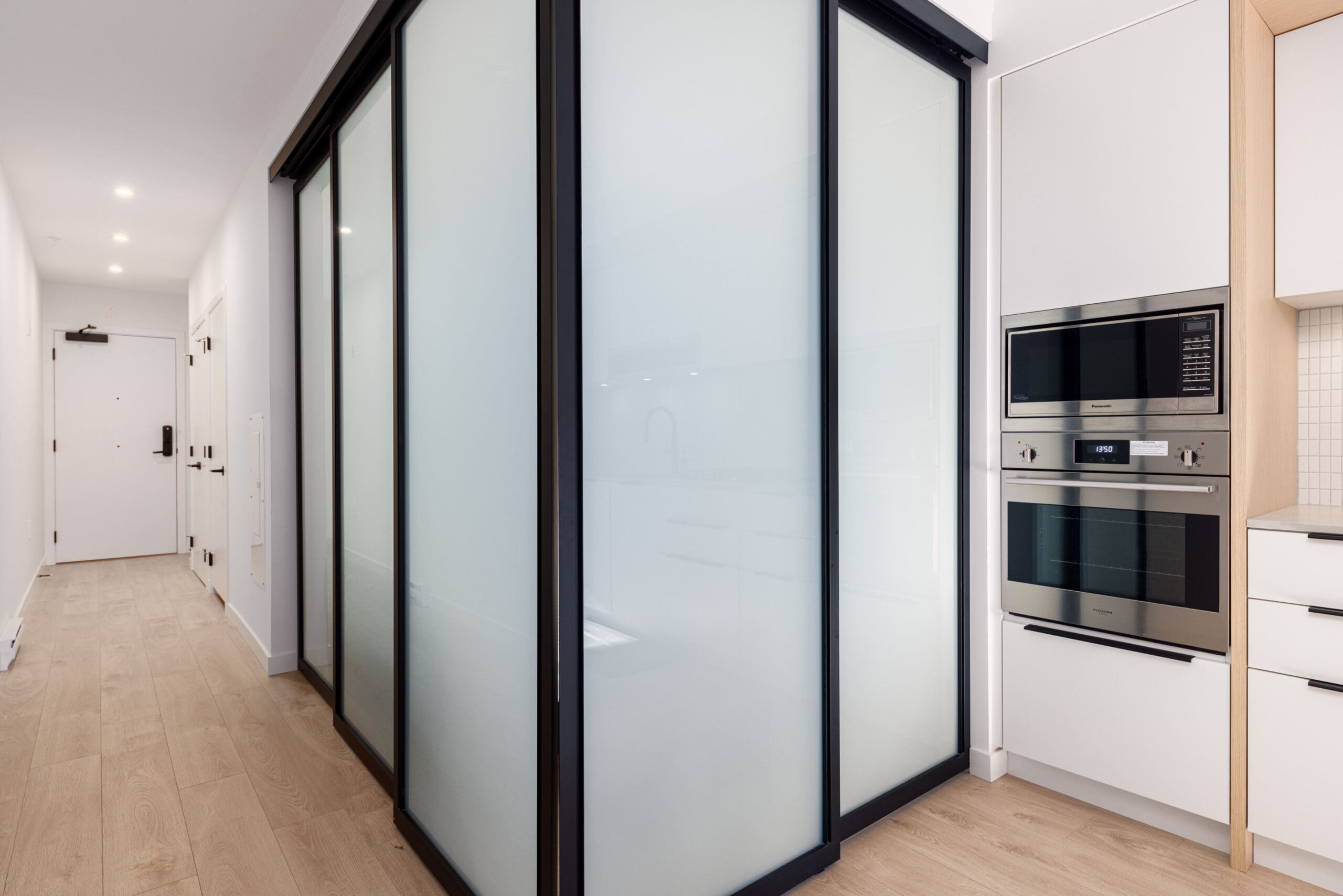 Modern kitchen with wood flooring, frosted glass sliding doors, built-in oven, and microwave.