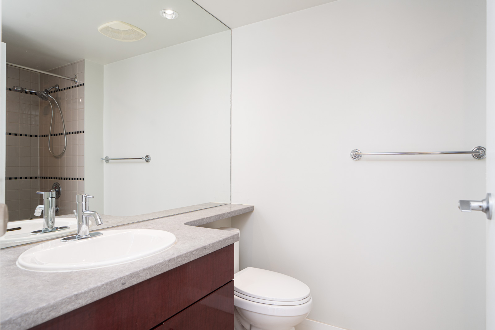 Modern bathroom with a large mirror, countertop sink, toilet, walk-in shower, towel bar, and neutral color scheme.