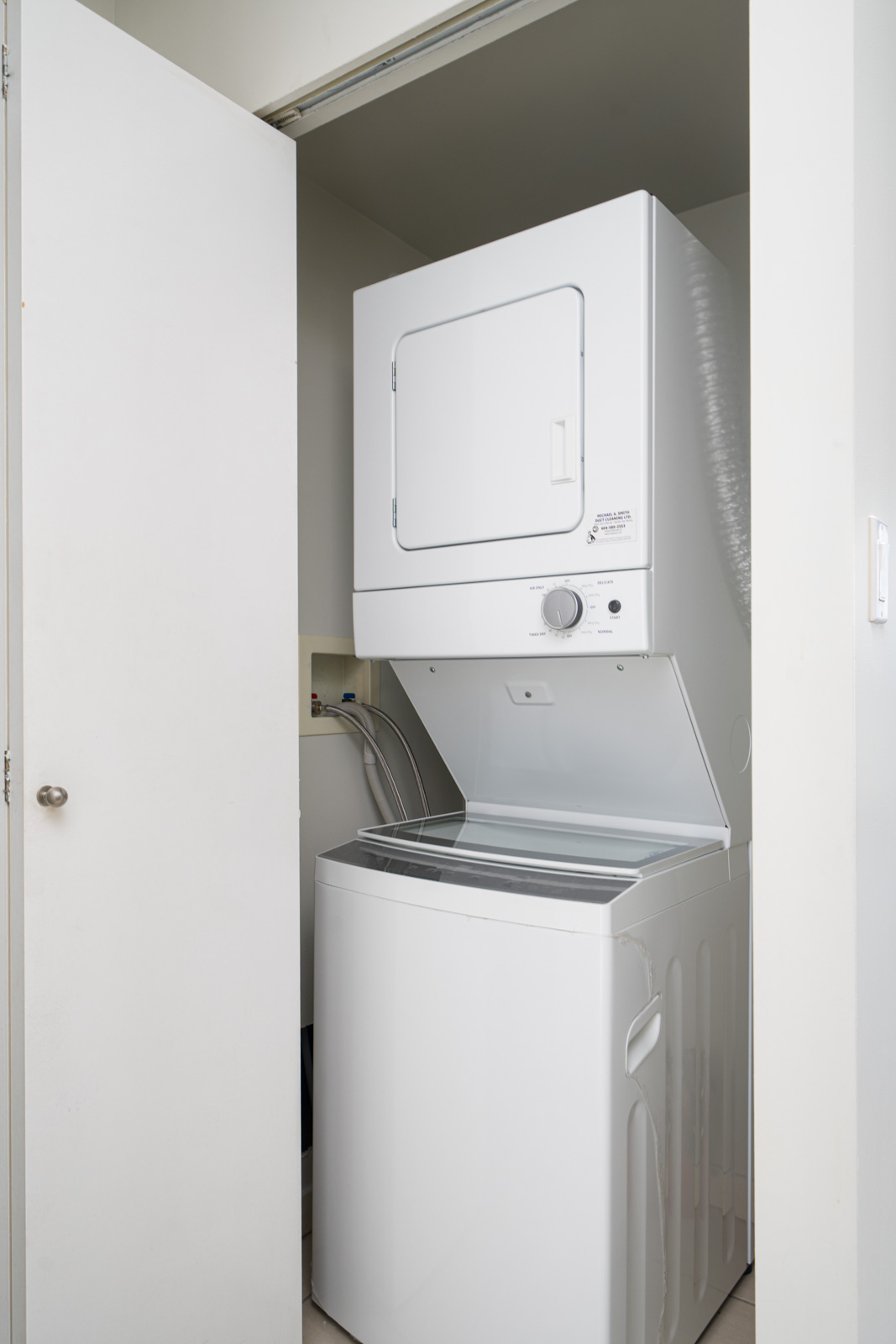 A white stacked washer and dryer unit is placed in a small laundry closet with an open door.