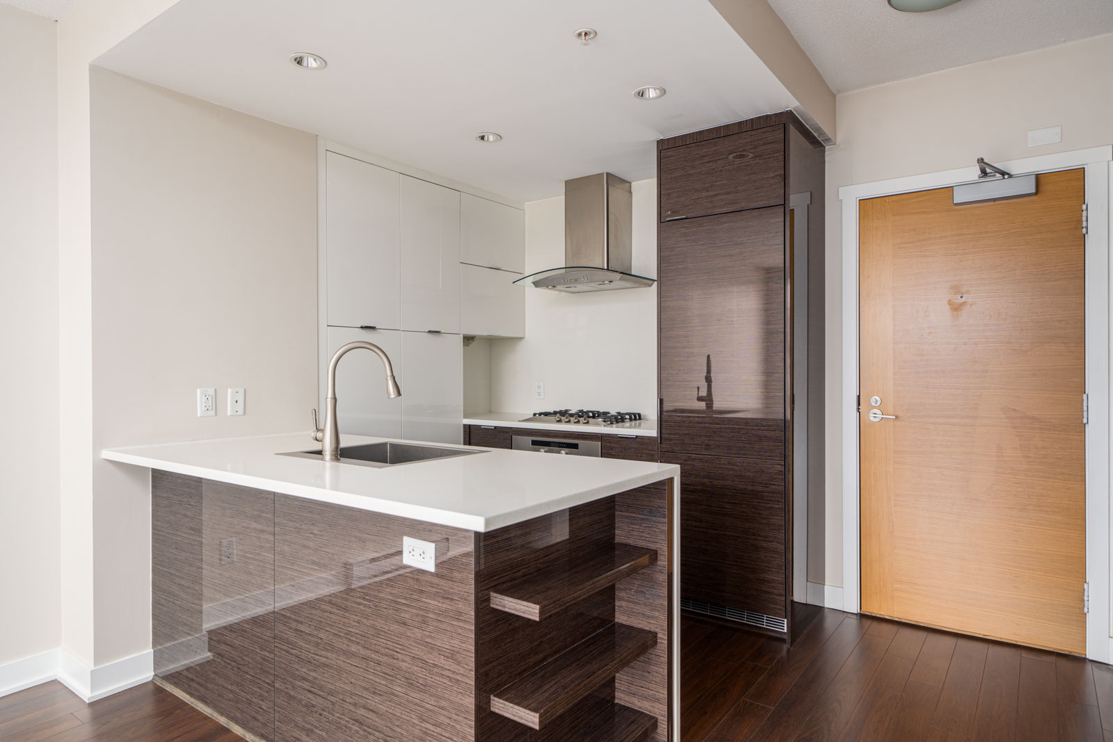 Modern kitchen with dark wood cabinets, white countertops, an island with a sink, and stainless steel appliances.