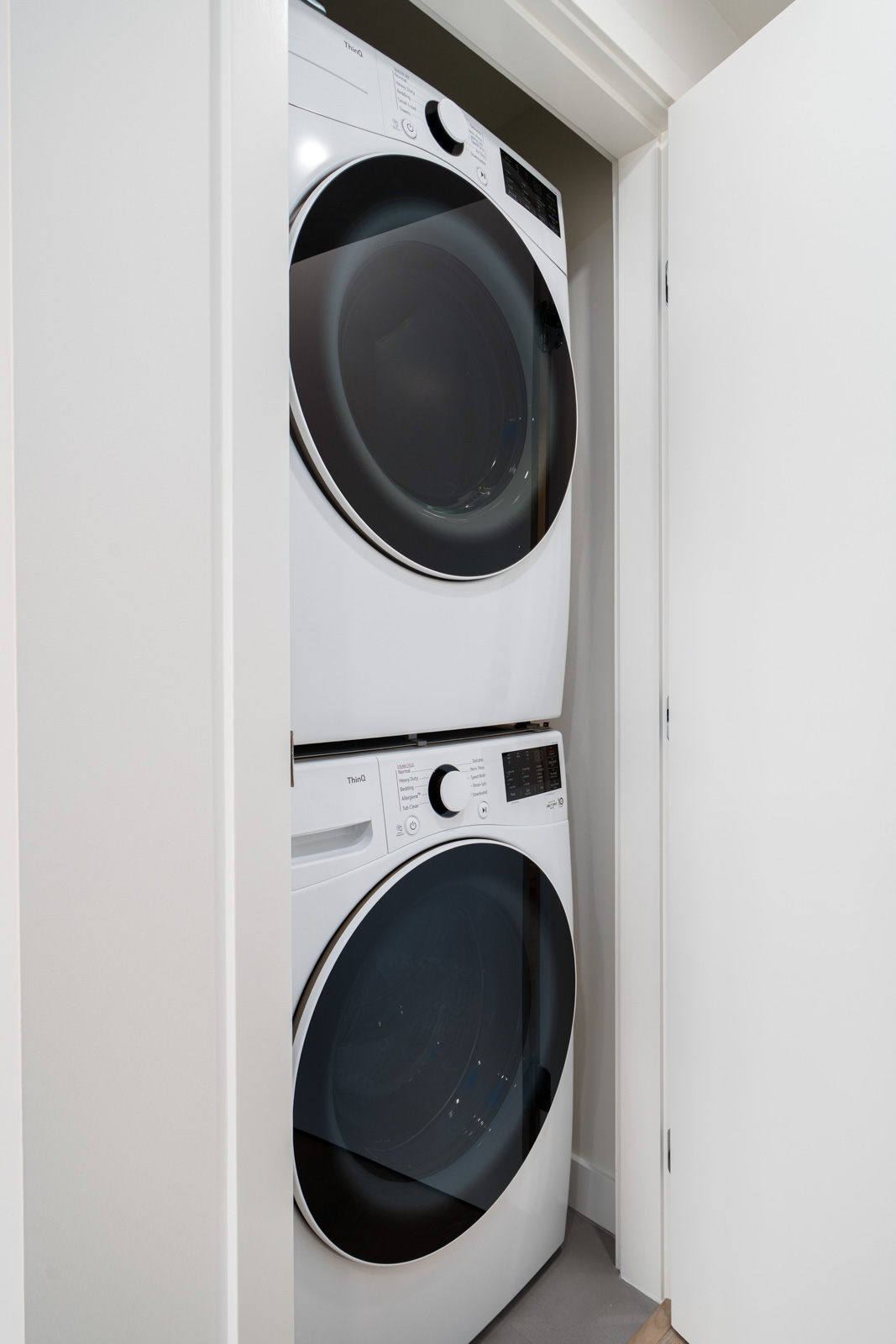 Stacked white washer and dryer inside a small closet with open white doors.