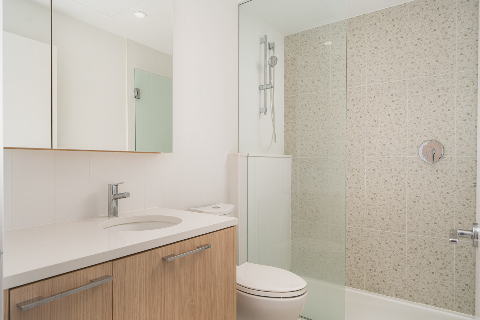 Modern bathroom with a glass-enclosed shower, white countertop with a sink, wooden cabinets, and a toilet.