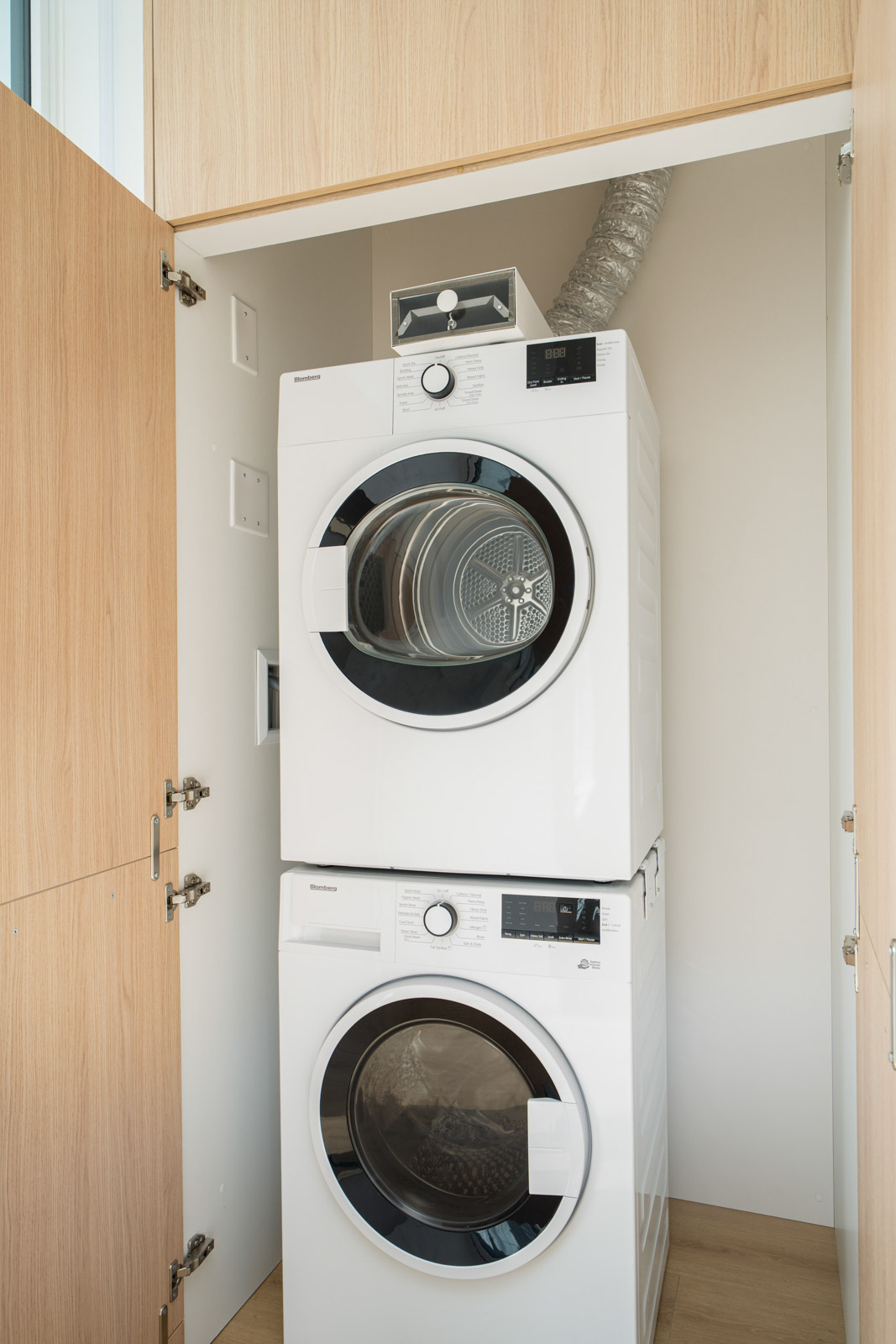 Stacked washer and dryer in a wooden closet with doors open. Dryer is on top, washer below. A small box is placed on the dryer.