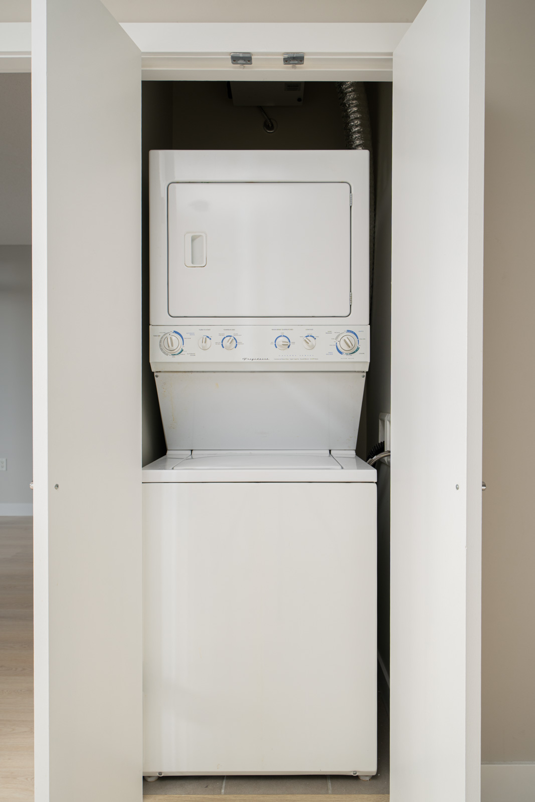 Stacked white washer and dryer unit behind partially open white closet doors.