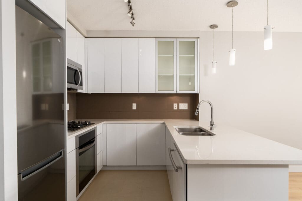 Modern kitchen with white cabinets, stainless steel appliances, a microwave above the stove, and a sink on a large island. Pendant lights hang from the ceiling.