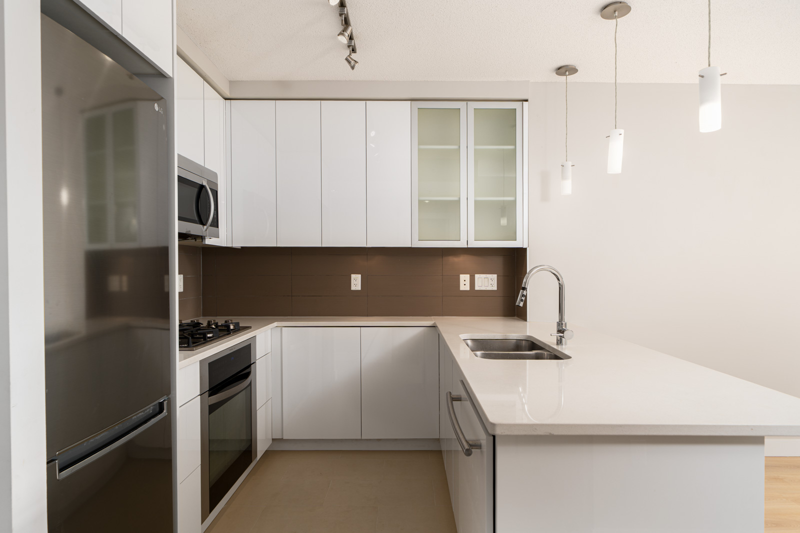Modern kitchen with white cabinets, stainless steel appliances, a microwave above the stove, and a sink on a large island. Pendant lights hang from the ceiling.