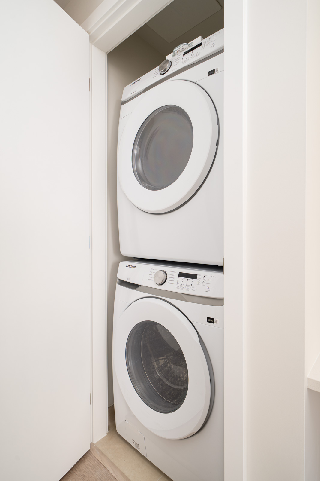 Stacked white washer and dryer in a narrow laundry closet with a partially open door.