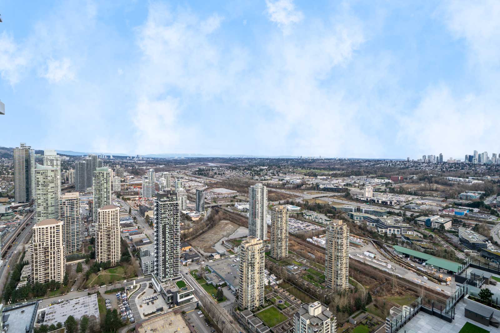 Aerial view of a cityscape with numerous high-rise buildings, roads, and greenery under a partly cloudy sky.